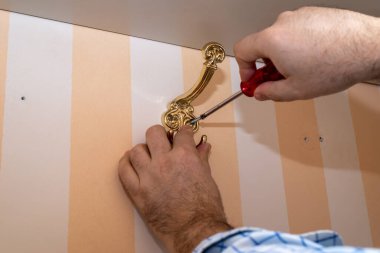 Dekoratif gardırop kancası takarken tornavida kullanan bir adam