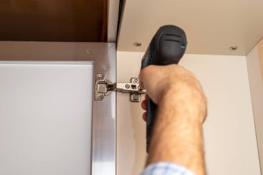 Gardırop kapağı menteşesini ayarlarken tornavida kullanan bir adam.