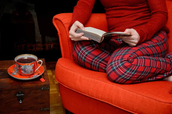 Lady reading and drinking tea by the fireplace — Stock Photo, Image