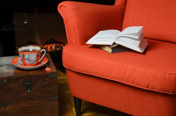 Books on armchair with cup of the by the fireplace — Stock Photo, Image