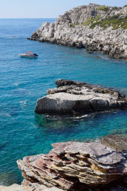 Gök mavisi denizde ıssız bir tekne. Sudan çıkan kayaların arasında.  