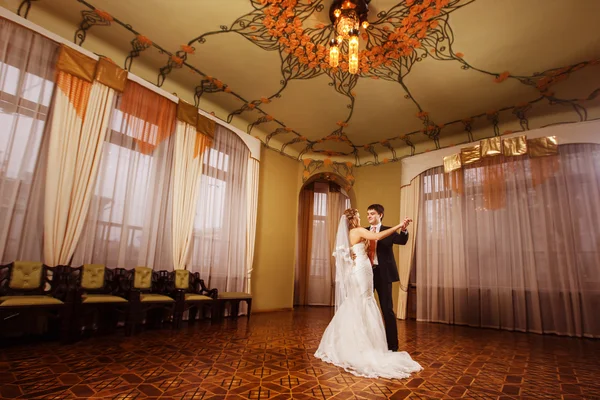 Wedding dance of a beautiful wedding couple in a stunning vintage spacious hall with wooden parquet and pattern ceiling.