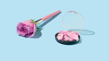 Pembe gül çiçekli makyaj fırçası ve parlak mavi arka planda taç yapraklarından oluşan yaratıcı bir kompozisyon. Son moda organik kozmetik ve moda konsepti.