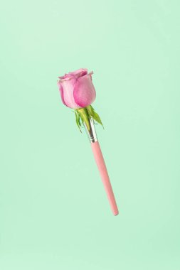 Yeşil nane arkaplanına karşı pembe gül makyaj fırçasından yapılmış moda bir kompozisyon. Kopya alanı ile en düşük moda kavramı.