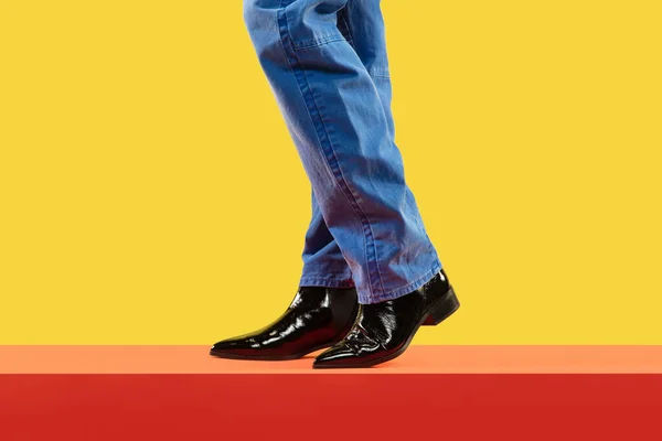 Mladý módní muž nohy v modrých džínách a černé boty na červené podlaze — Stock fotografie