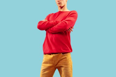 Mavi stüdyo arka planında poz veren parlak renkli elbiseli genç adam..