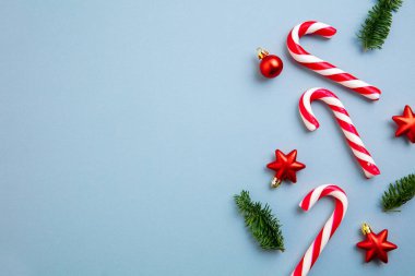 Noel süsleri, baston şekerler ve kırmızı yıldızlar mavi arka planda..