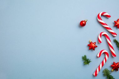 Noel süsleri, baston şekerler ve kırmızı yıldızlar mavi arka planda..