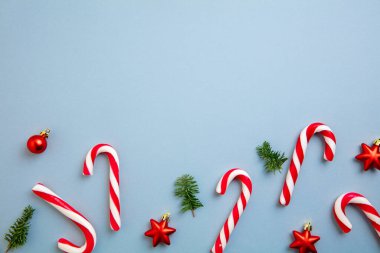 Noel süsleri, baston şekerler ve kırmızı yıldızlar mavi arka planda..