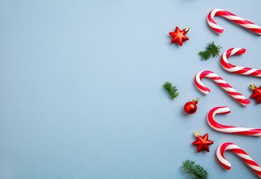 Noel süsleri, baston şekerler ve kırmızı yıldızlar mavi arka planda..