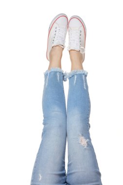 Beyaz arka planda izole edilmiş kot pantolon ve spor ayakkabılı kadın bacakları.