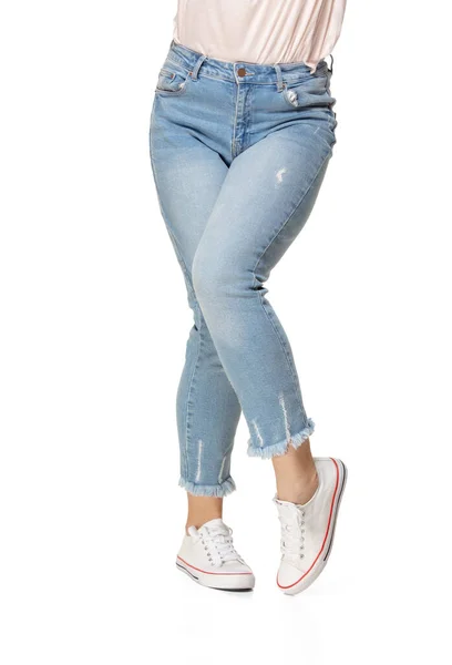Mavi kot pantolon ve beyaz arka planda izole spor ayakkabı giyen ince kadın bacakları. — Stok fotoğraf