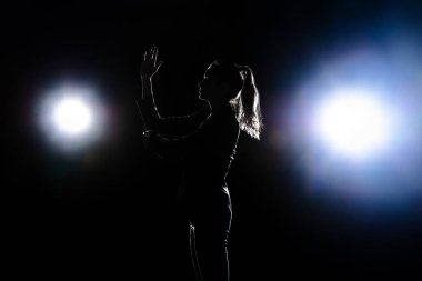 Karanlık arka planda yalnız poz veren üzgün kadın silueti.