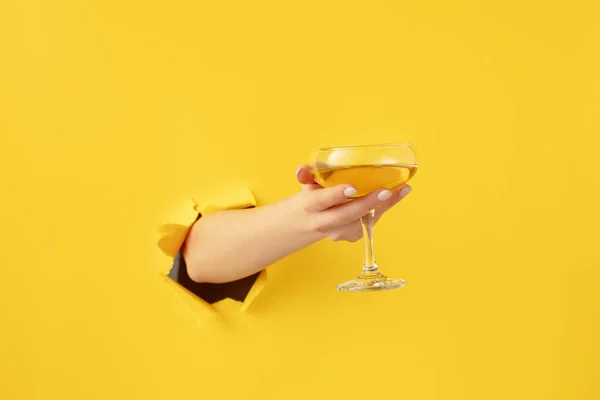 Kvinna hand med cocktail glas bryter igenom gul papper bakgrund. — Stockfoto