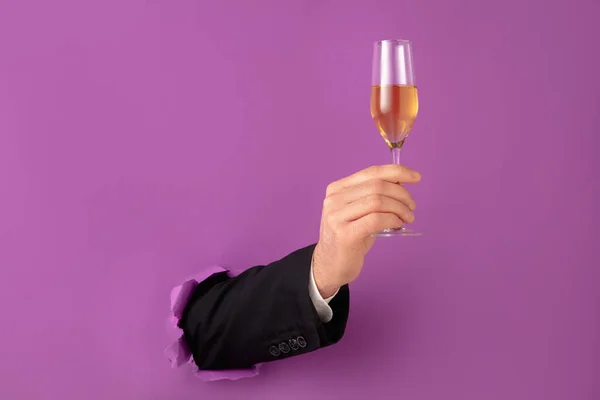 La mano masculina que sostiene la flauta de champán rompe el fondo púrpura — Foto de Stock