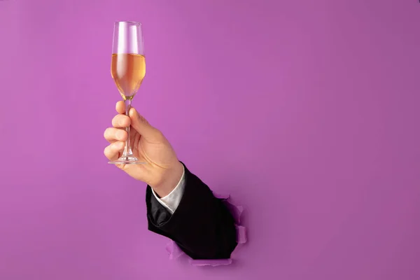 La mano masculina que sostiene la flauta de champán rompe el fondo púrpura — Foto de Stock