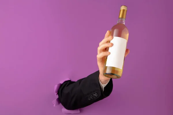 Mão masculina segurando garrafa de vinho e rompendo fundo de papel roxo. — Fotografia de Stock