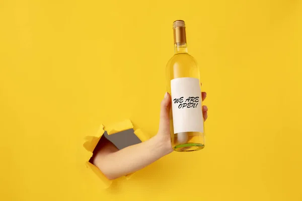 Mão humana segurando garrafa de vinho com colarinho aberto isolado no fundo amarelo — Fotografia de Stock