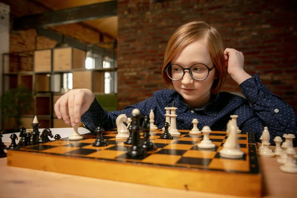 Мальчик в очках сидит дома и играет в шахматы в одиночку. — стоковое фото