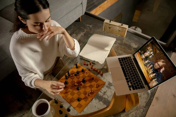 Молодая красивая девушка сидит дома и играет в шахматы с другом онлайн. — стоковое фото