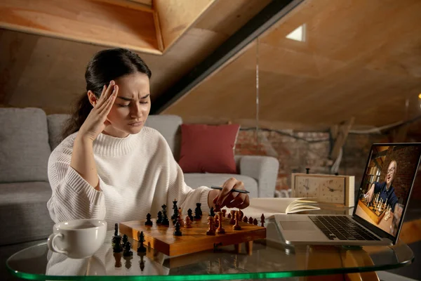 Молодая красивая девушка сидит дома и играет в шахматы с другом онлайн. — стоковое фото