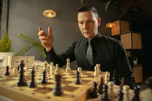 Серьезный шахматист сидит дома и играет в шахматы в одиночку. — стоковое фото