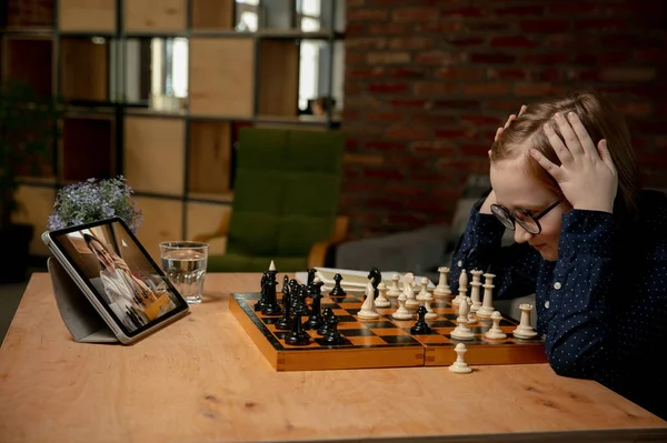 Умный маленький кавказский шахматист играет в шахматы онлайн с помощью ноутбука. — стоковое фото