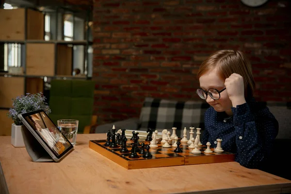 Серьезная маленькая кавказская шахматистка, играющая в шахматы онлайн на ноутбуке. — стоковое фото