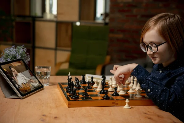 Серьезная маленькая кавказская шахматистка, играющая в шахматы онлайн на ноутбуке. — стоковое фото