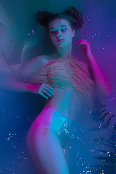 Portrait de jeune belle fille adorable posant dans l'eau dans la lumière néon moderne. — Photo
