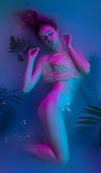 Portrait de jeune belle fille adorable posant dans l'eau dans la lumière néon moderne. — Photo