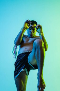 Tayland boksu eğitimi alan bir adam mavi arka planda neon ışığında.