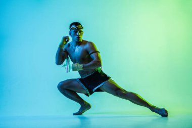 Tayland boksu eğitimi alan bir adam mavi arka planda neon ışığında.