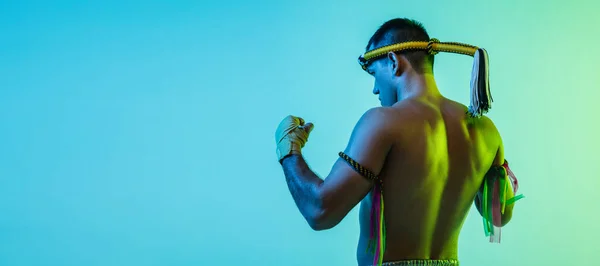 Young man thai boxer posing over blue background in neon light.