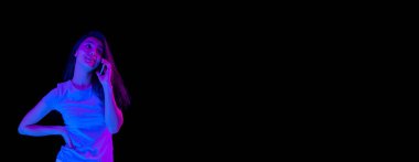 Genç ve güzel bir kız telefonda konuşuyor. Karanlık arka planda, neon ışıkta..