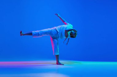 Mavi arka planda beyaz giysili hip-hop dansı yapan, neon ışıklı kız.
