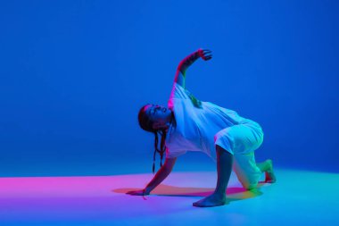 Mavi arka planda beyaz giysili hip-hop dansı yapan, neon ışıklı kız.