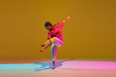 Neon ışıklı arka planda kırmızı beyaz elbiseyle hip-hop yapan sportif kız..