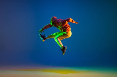 Genç erkek dansçı mavi arka planda neon ışıkta tek başına zıplıyor.