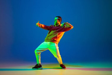 Genç adam neon ışıkta mavi arka planda hip-hop dansı yapıyor.