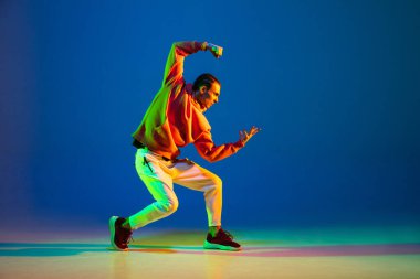 Genç erkek dansçı mavi arka planda yalnız poz veriyor.