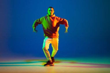 Genç hip-hop dansçısı mavi arka planda tek başına neon ışıkta dans ediyor.
