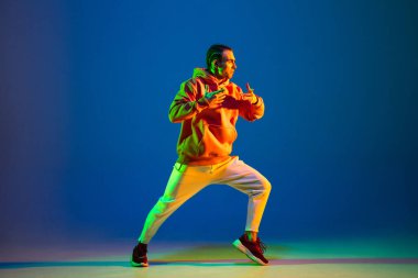 Genç adam neon ışıkta mavi arka planda hip-hop dansı yapıyor.
