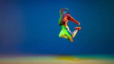 Genç adam neon ışıkta mavi arka planda hip-hop dansı yapıyor.