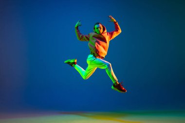 Genç erkek dansçı mavi arka planda neon ışıkta tek başına zıplıyor.