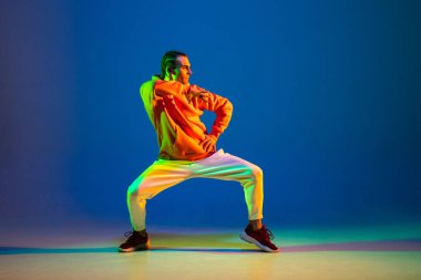 Genç hip-hop dansçısı mavi arka planda, neon ışıkta tek başına dans ediyor.