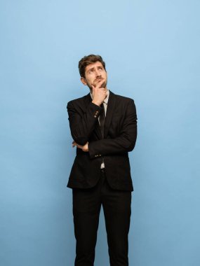 Mavi arka planda izole edilmiş siyah takım elbiseli beyaz bir adamın portresi..