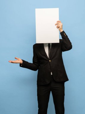 Siyah takım elbiseli, mavi arka planda boş bir kağıt parçası olan genç bir adam..
