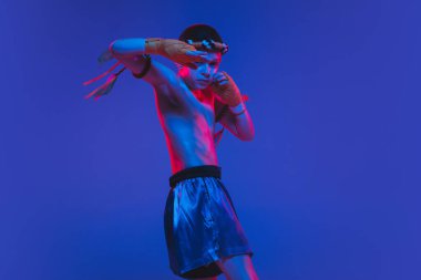 Genç Taylandlı boksör mavi arka planda neon ışıkta eğitim görüyor..