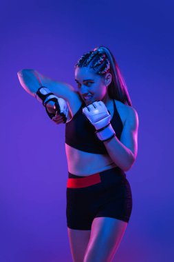 Atletik bayan MMA dövüşçüleri mavi-pembe arka planda neon ışıkta eğitiliyor.